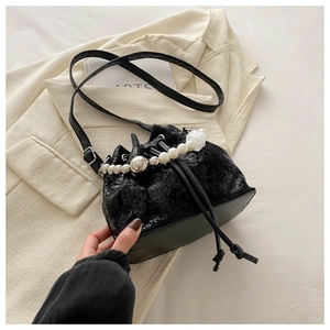Detail of black patent leather bucket bag with decorative pearl chain and drawstring closure