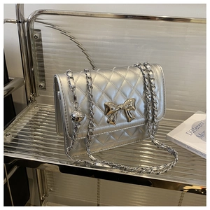 Detailed view of silver quilted crossbody bag with a metallic bow clasp and chain strap