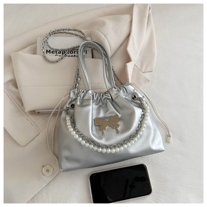Detail of silver drawstring bucket bag featuring pearl chain and butterfly metal ornament