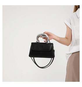 Détail d'un sac en cuir noir avec une poignée moderne en métal argenté et une texture grainée