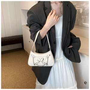 Detalle del bolso de hombro blanco con mariposa de metal plateado y elementos de cadena