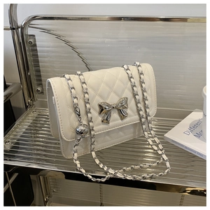 Macro shot of white quilted leather texture with oversized silver bow and metal chain