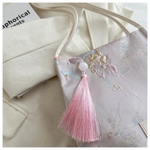 Détail du sac en soie brodée rose avec motifs floraux, fil doré et pompon en soie