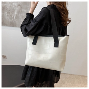Close-up of white geometric patchwork tote bag shown on model with black shoulder strap
