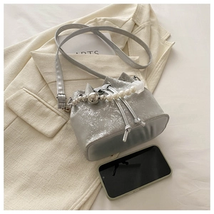 Detailed view of silver glitter bucket bag with pearl chain handle on beige blazer