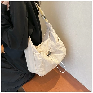Detail of a large beige nylon crossbody bag featuring stylish pleats and a wide strap