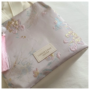 Détail d'un sac en soie rose avec broderie florale, fils dorés et long pompon