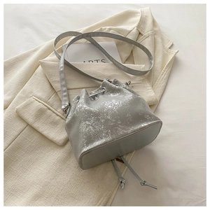 Detail of silver textured bucket bag with drawstring closure on a beige blazer