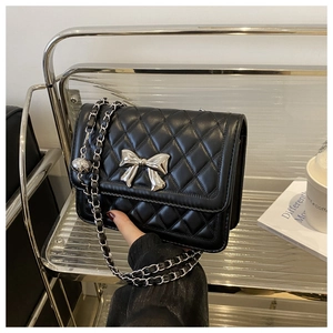 Detail of black quilted shoulder bag featuring silver metal bow and chain strap accents