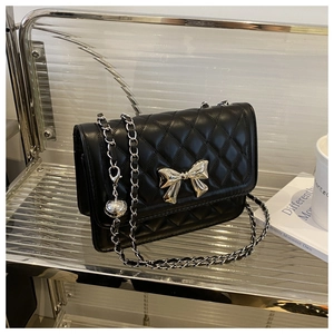 Detail of black quilted shoulder bag with silver bow clasp and woven chain strap