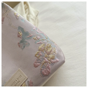 Détail de la broderie sur brocart rose avec étiquette en cuir sur un sac seau