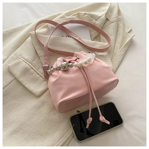 Detail of pink drawstring bucket bag with pearl handle on a textured blazer background
