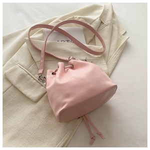 Pink drawstring bucket bag with tassels laid on a beige blazer for fashion styling