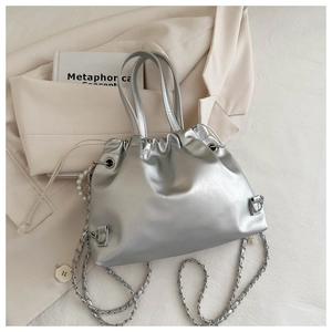 Detail of silver drawstring bucket bag featuring pearl charm and metal chain strap
