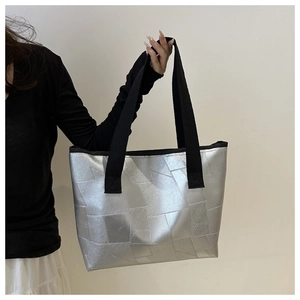 Detail of silver tote bag with geometric patchwork texture and black shoulder strap
