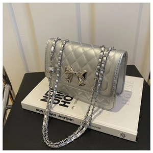 Detail of silver quilted crossbody bag featuring metal bow and woven chain strap