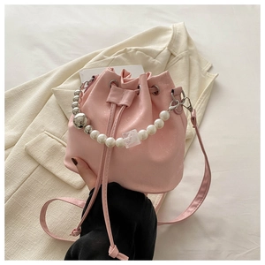 Close-up of pink bucket bag with pearl and silver metal bead handle on beige background