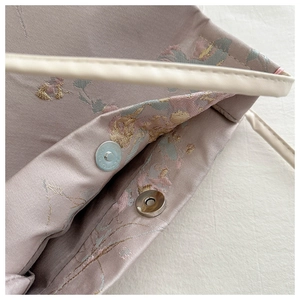 Détail du sac brodé en satin lilas montrant le fermoir magnétique et les motifs floraux