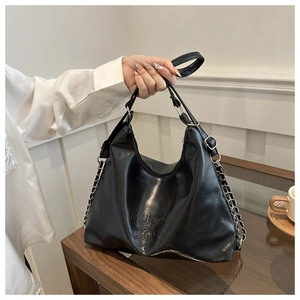 Detail of black faux leather tote with embossed logo lettering and metal chain strap