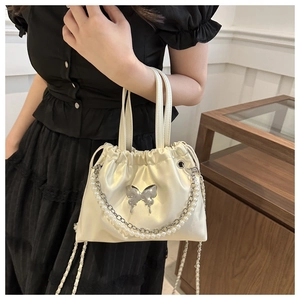 Detail of cream drawstring bucket bag with silver butterfly buckle and pearl chain strap