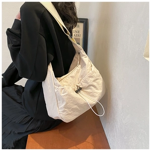 Detail of cream nylon crossbody bag showing drawstring detail and wide strap on model