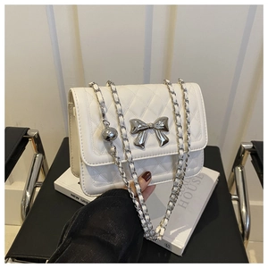 Close-up of white quilted leather crossbody bag with silver metal bow and chain strap