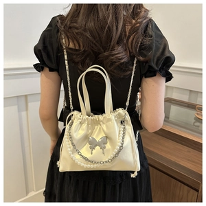 Detail of a creamy white satin drawstring bag with a silver butterfly and pearl chain