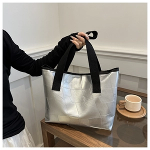 Detail of silver geometric tote bag with textured panels on a dark wooden table