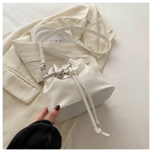 Detail of cream white bucket bag with pearl handle and drawstring closure on beige blazer
