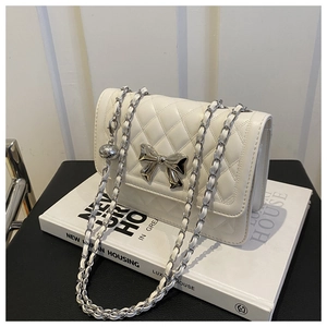 Macro view of white quilted faux leather bag with silver bow clasp and chain strap detail