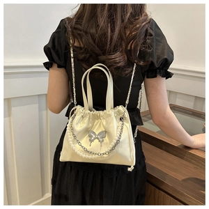 Detail of cream satin bucket bag with silver metal butterfly and pearl chain strap
