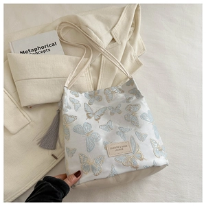 Détail du sac cabas brodé de papillons avec pompon gris et patch logo en cuir