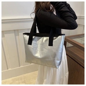 Silver metallic tote bag with geometric stitching and wide black strap on model