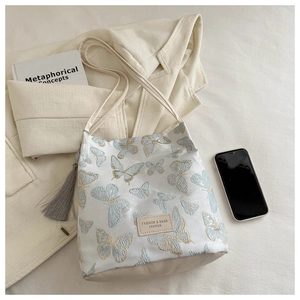 Détail de broderie papillon bleu et base en cuir sur un sac fourre-tout beige