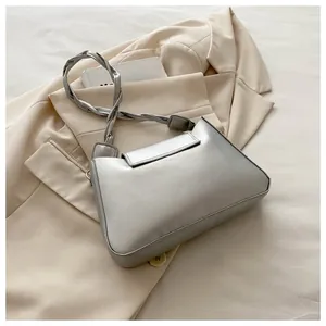Detail of silver metallic shoulder bag with woven strap on a beige blazer background