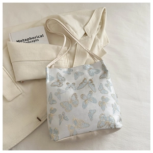 Gros plan d'une broderie papillon bleue sur un grand sac cabas en satin beige