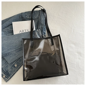 Détail d'un sac cabas transparent en PVC avec pochette noire sur fond blanc texturé