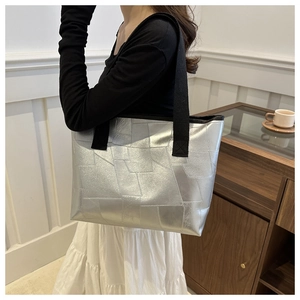 Detail of silver metallic tote bag with geometric textured panels and black woven straps