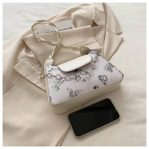 Detail of cream shoulder bag featuring black butterfly prints and a decorative metal chain