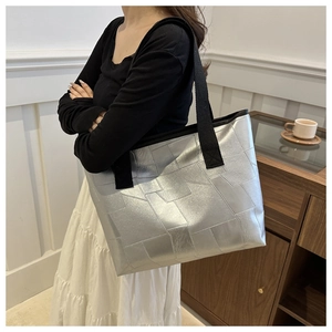 Metallic silver tote bag with geometric texture and black strap in a cozy cafe setting