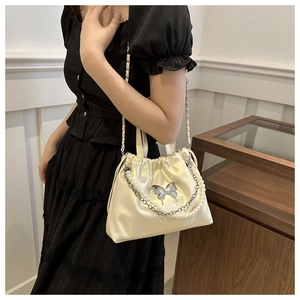 Detail of a creamy satin drawstring handbag featuring a silver butterfly clasp and pearl chain