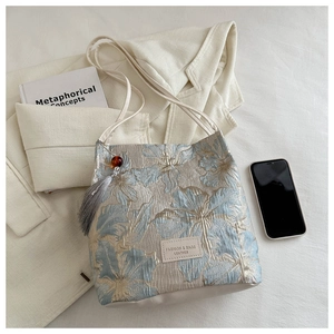 Détail du tissu jacquard floral sur un sac bleu avec un pendentif à franges gris raffiné