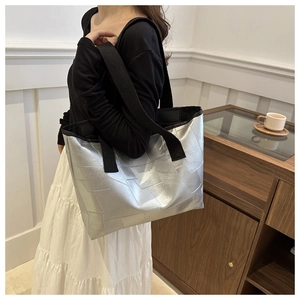 Side view of a silver metallic tote bag with wide black shoulder straps for daily commute