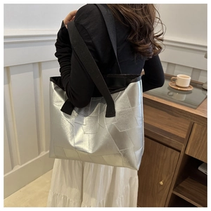 Detailed view of silver geometric tote bag with black canvas straps on shoulder
