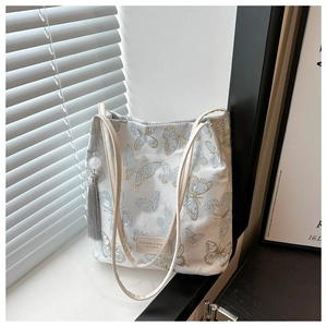 Détail de broderie papillon jacquard sur sac fourre-tout blanc avec breloque à pompon