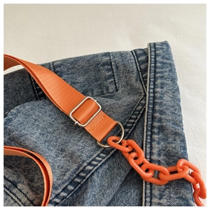 Detailed close-up of blue denim bag with orange nylon strap and matching acrylic chain