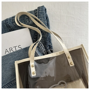 Détail d'un sac cabas transparent avec bordure crème, rivets dorés et pochette interne