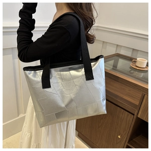 Detail of silver geometric tote bag with metallic finish and wide black shoulder strap