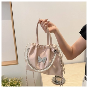 Detail of pink bucket bag featuring pearl handle, butterfly clasp and metal chain strap