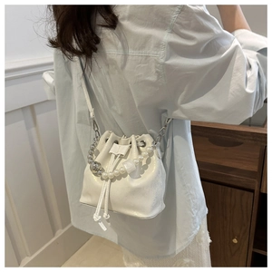 Detail of white pearlescent bucket bag with pearl handle and crossbody strap shown on model